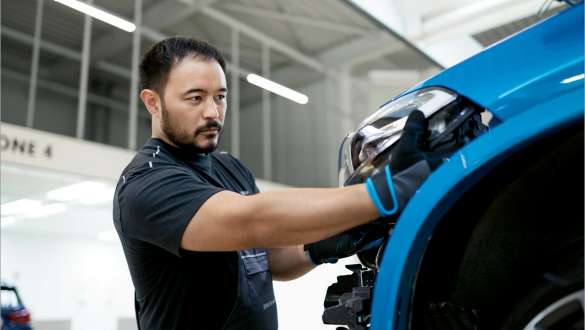 Man installs headlights on a BMW Man installs a headlight in a blue BMW in a production hall