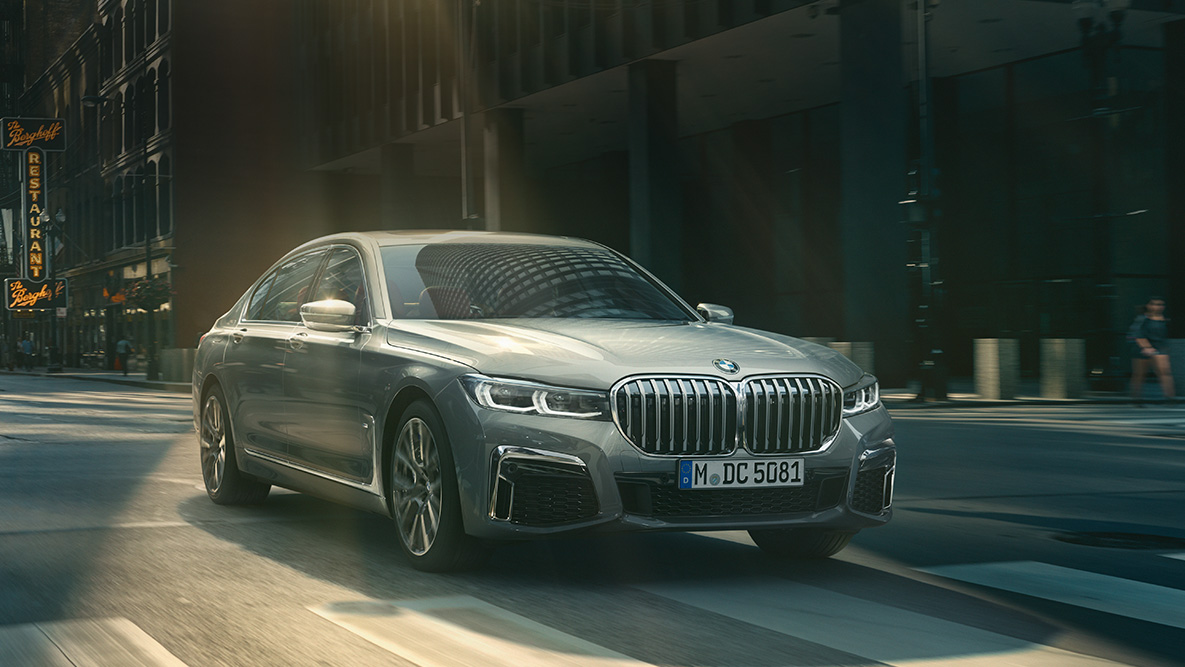 Driving Assistant Professional: three-quarter front view of BMW 7 Series Sedan G11 driving in front of urban setting Driving Assistant Professional: three-quarter front view of BMW 7 Series Sedan G11 driving in front of urban setting