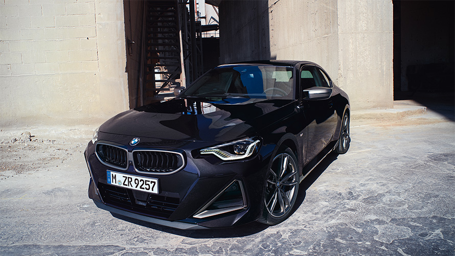 BMW M240i xDrive Coupé G42 2021 Black Sapphire metallic three-quarter front view standing in front of warehouse