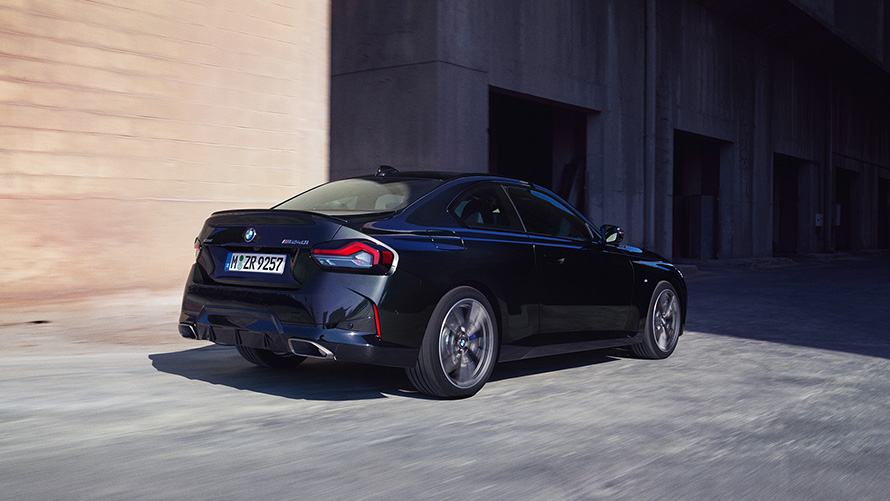 BMW M240i xDrive Coupé G42 2021 Black Sapphire metallic three-quarter rear view standing in front of warehouse