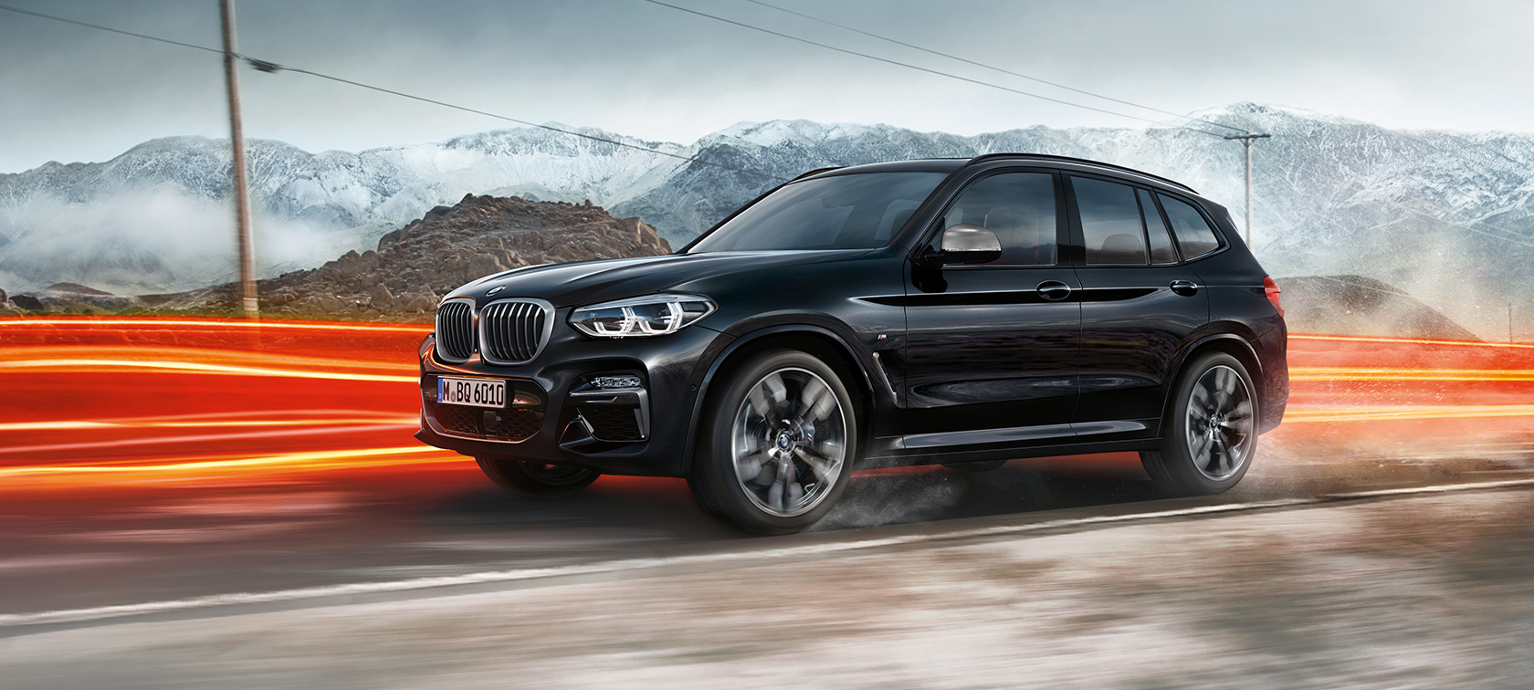 BMW X3 M40i and BMW X3 M40d SUV, side view F97. BMW X3 M40i and BMW X3 M40d SUV in Black Sapphire metallic, driving, exterior, side view in front of mountain scenery with light strips F97.