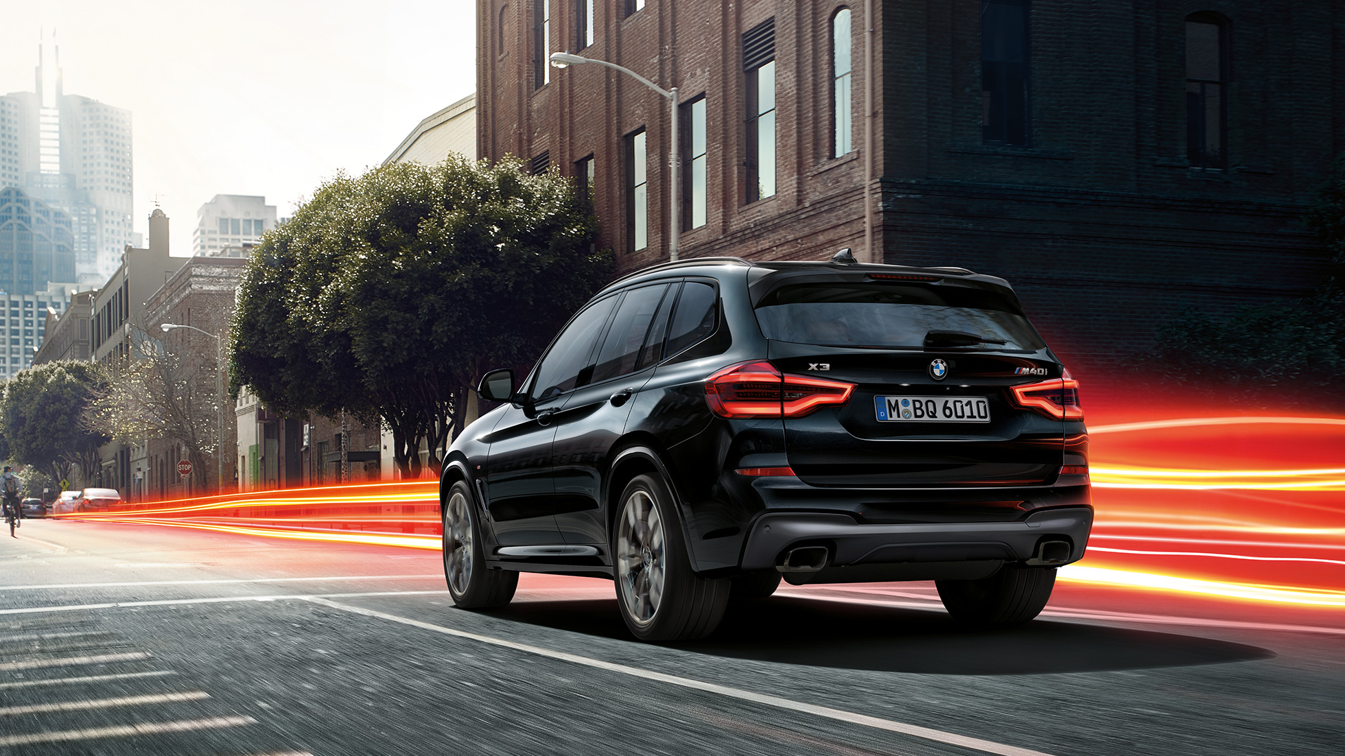 BMW X3 M40i SUV, three-quarter rear view F97. BMW X3 M40i SUV in Black Sapphire metallic, driving, exterior, three-quarter rear view before an urban background with light strips F97.