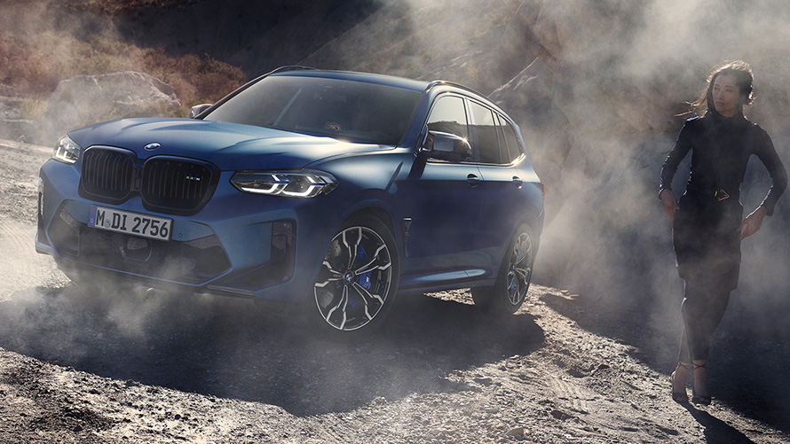 BMW X3 M Competition F97 LCI 2021 three-quarter front view standing in stony terrain BMW X3 M Competition F97 LCI Facelift 2021 Frozen Marina Bay Blue metallic three-quarter front view standing in stony terrain with female model