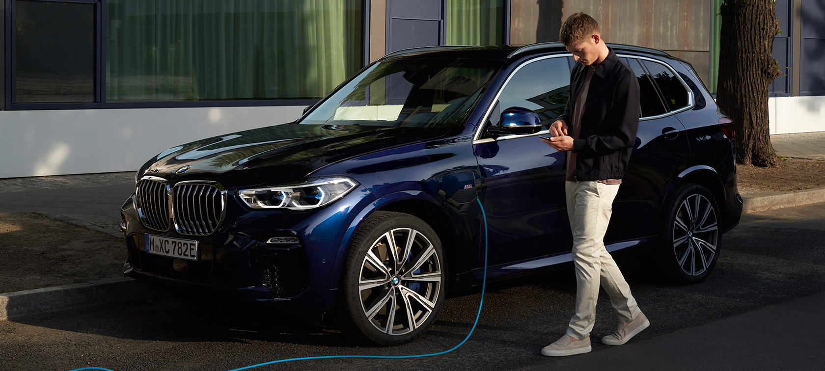 Man uses My BMW App on smartphone Man uses My BMW App from BMW ConnectedDrive on smartphone while charging his BMW X5 Plug-in Hybrid