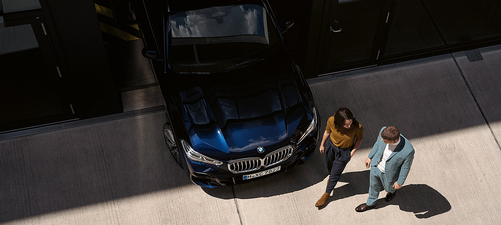Woman and man walk past the front of a BMW from bird's eye view
