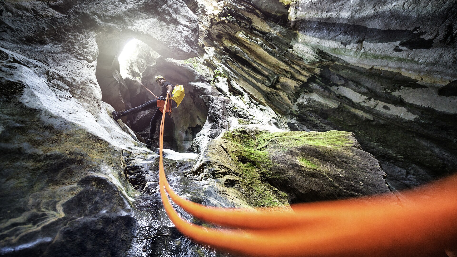 Tour di canyoning di uno sportivo con casco giallo e attrezzatura da canyoning durante il canyoning in Allgäu mentre scende da una parete