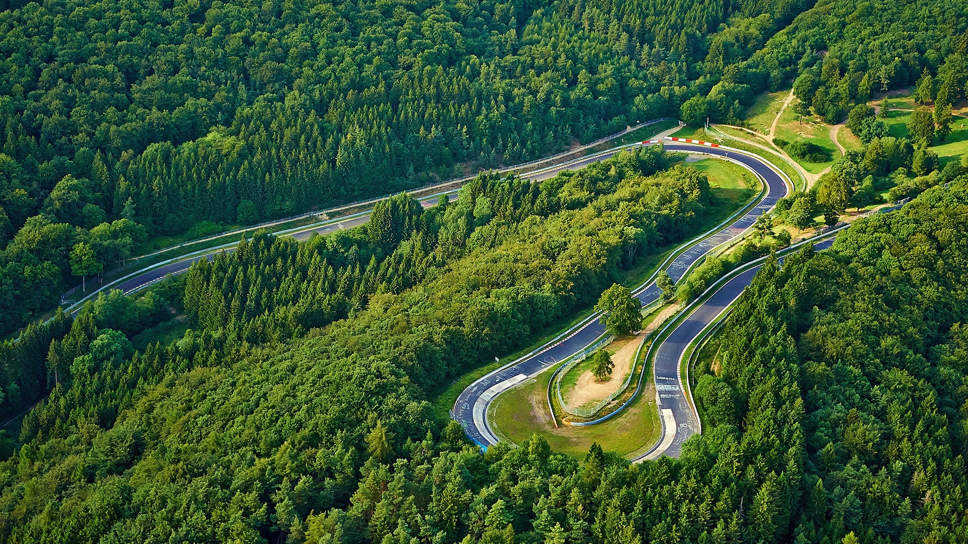 Dans le massif de l’Eifel, la boucle Nord du Nürburgring compte pas moins de 73 virages et sections de courbe. Leurs noms sont aussi prometteurs que les images auxquelles ils sont associés : la mine (« Bergwerk »), la queue d’hirondelle (« Schwalbenschwanz ») ou la petite fontaine (« Brünnchen »). Tous sont célèbres ou redoutés. Dans cet « enfer vert », le virage le plus emblématique s’appelle KARUSSELL (ou « carrousel Caracciola »). Cet étroit virage en U à gauche se glisse entre de hautes bordures. Ici, la piste n’est pas asphaltée mais revêtue de plaques de béton. Les pilotes abordent ce court tronçon irrégulier à 80 km/h seulement (suivant le véhicule), espérant trouver la trajectoire idéale afin de bénéficier du plus grand élan possible pour poursuivre en direction du Hohe Acht, le plus haut sommet du massif de l’Eifel.